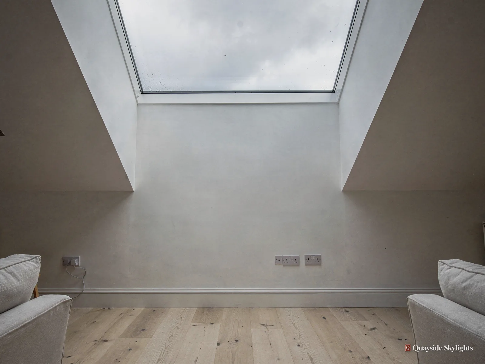 Empty white room with oak flooring lit by a large flat rooflight set in a deep ceiling well
