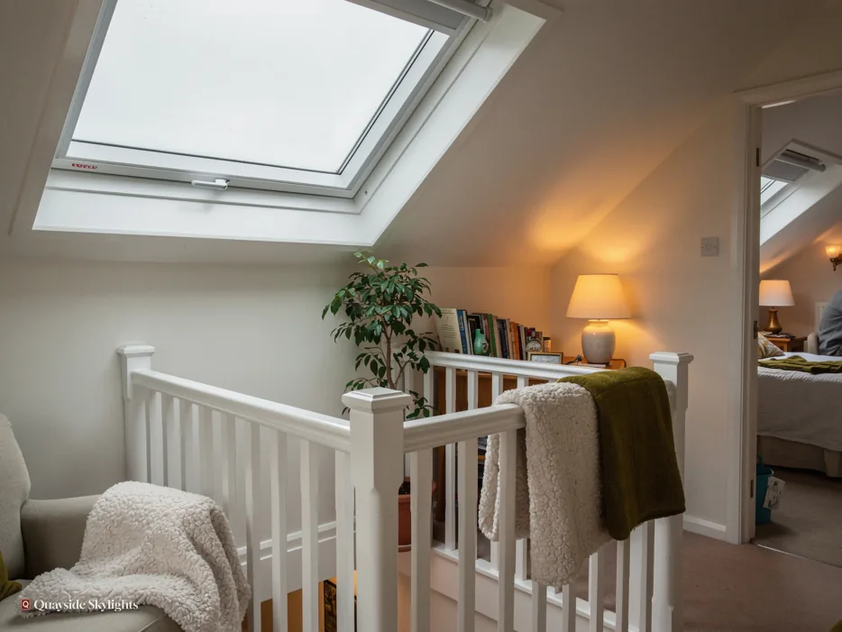 Cosy landing with a white roof window over a painted banister, a lamp and a houseplant