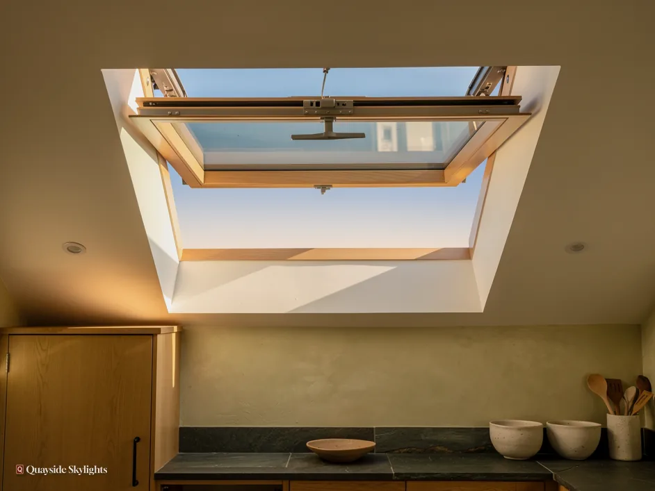 Kitchen ceiling with an opening roof window tilted open above a worktop and wooden bowls