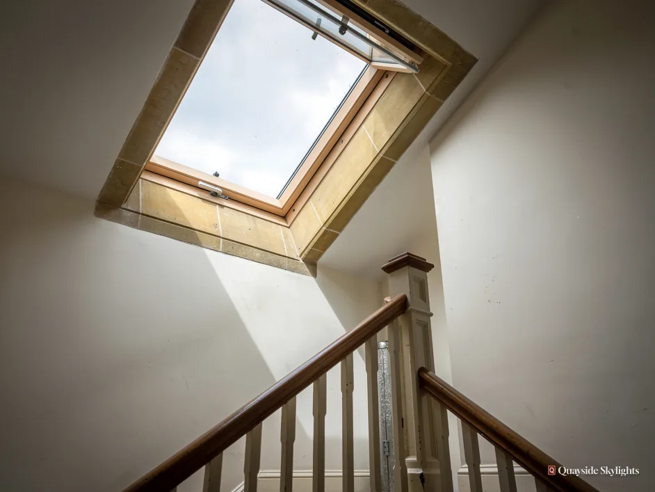 Stairwell with a pine roof window propped open above a white and oak staircase