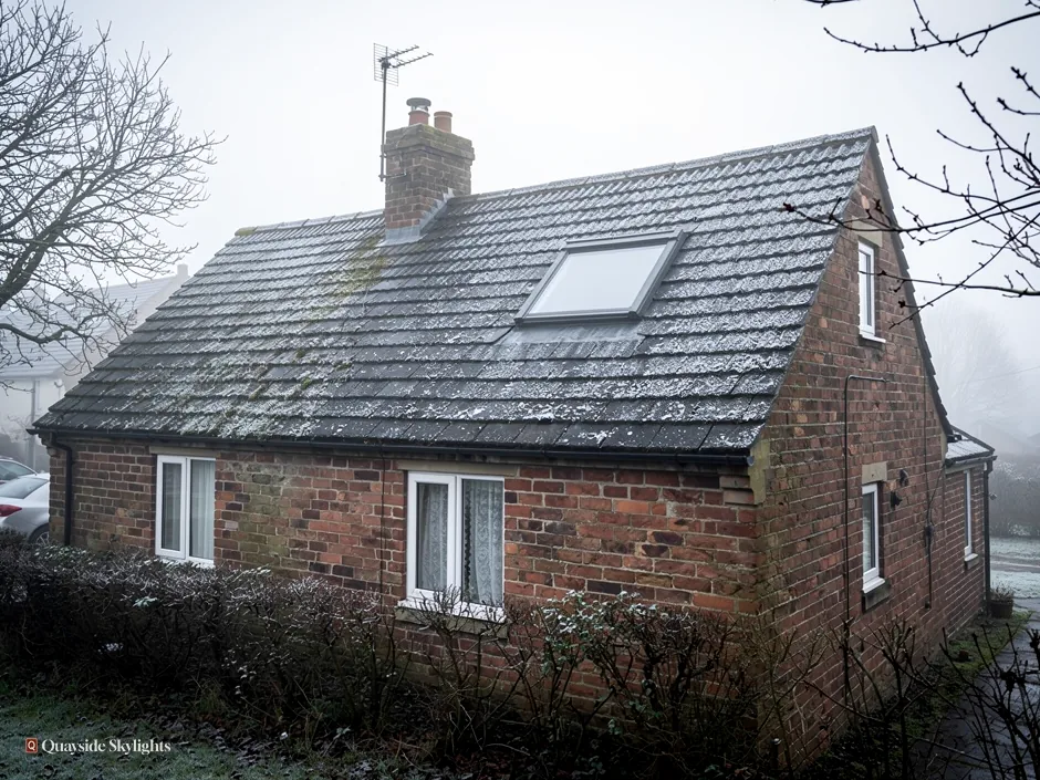 Red brick cottage with a slate roof, chimney and single roof window on a misty day