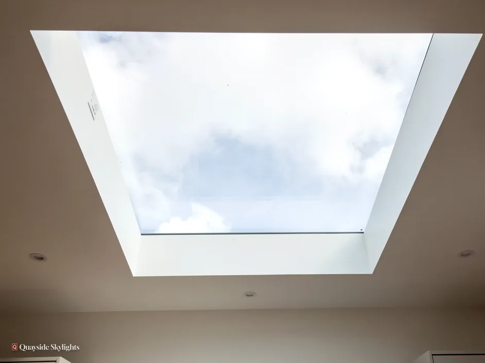 View up through a large square flat rooflight to a cloudy sky from a white room