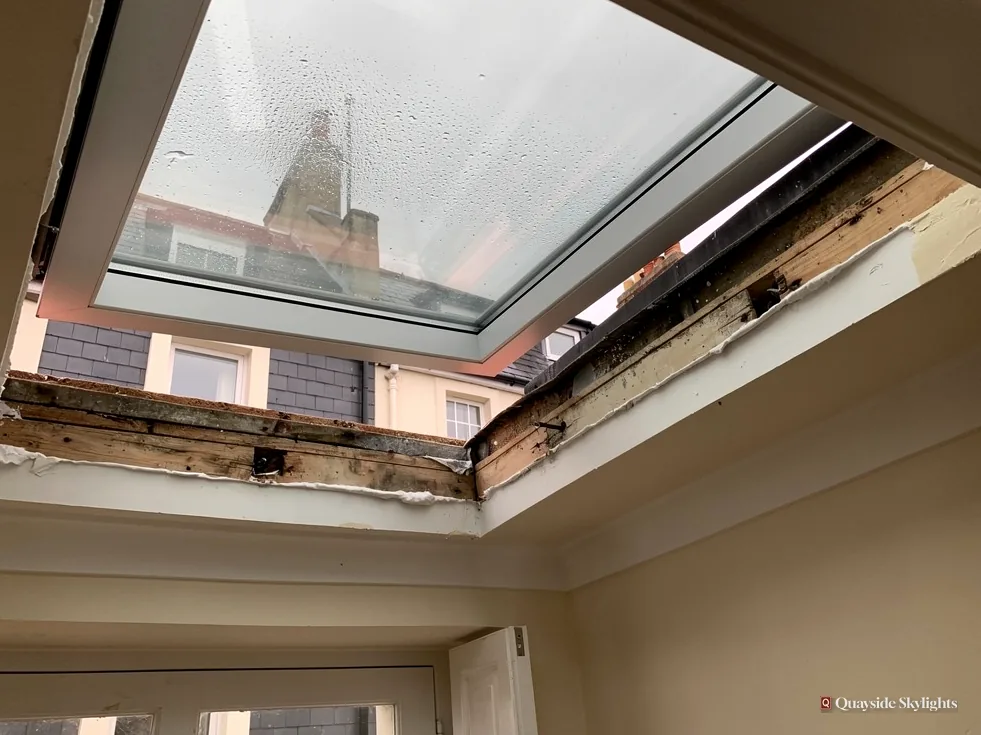 Old flat rooflight with condensation on the glass and a rotting timber upstand around the opening