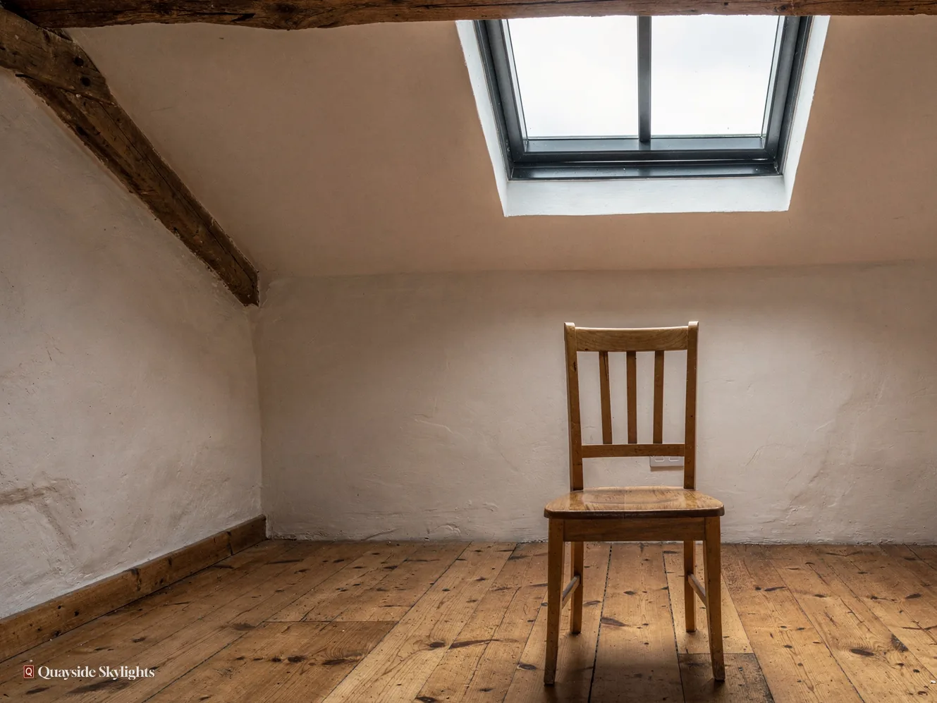 Whitewashed attic room with an old ceiling beam, a dark slim rooflight and a single wooden chair