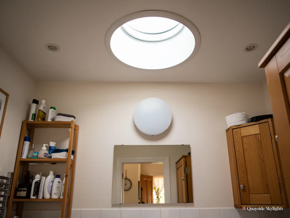 Small bathroom with a circular sun tunnel diffuser above a mirror and shelves of toiletries