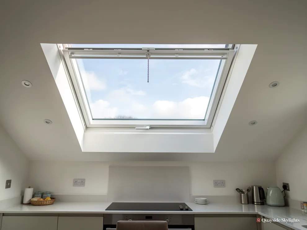 White opening rooflight above a kitchen hob with blue sky and cloud through the glass