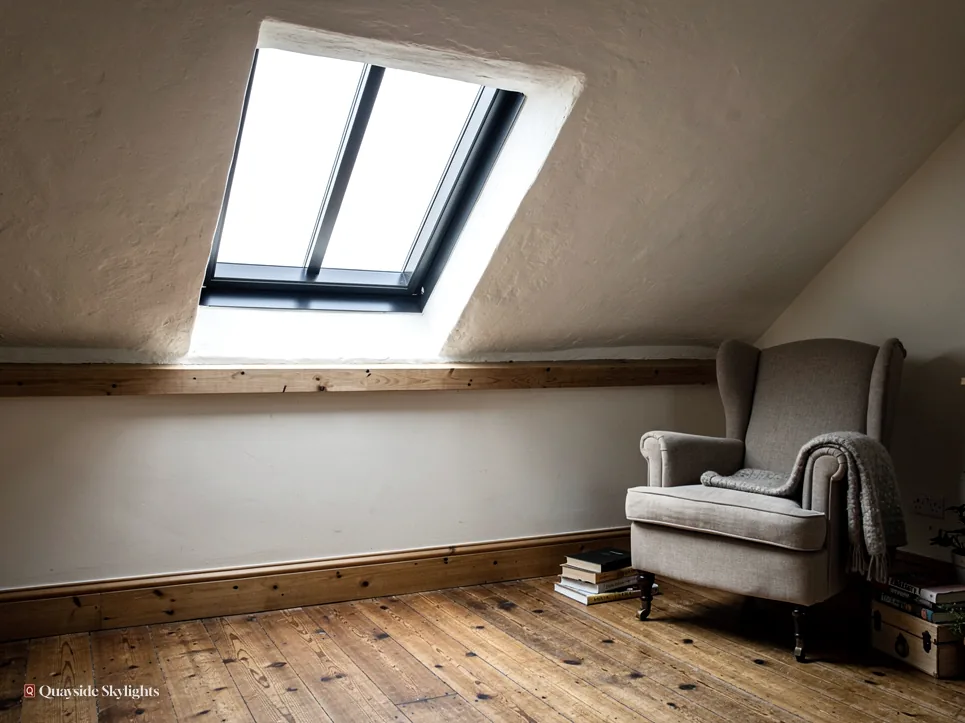 Slim dark-framed rooflight in a sloping ceiling above a grey wingback chair and timber floor
