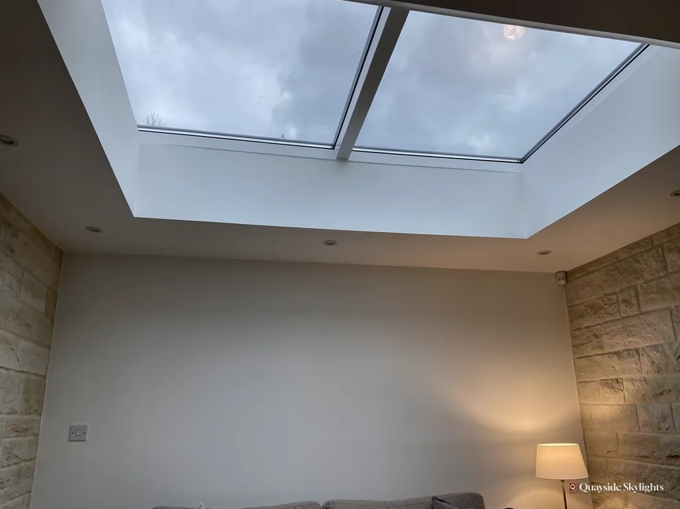 Large twin-pane flat rooflight lighting a plain room with a bare stone wall