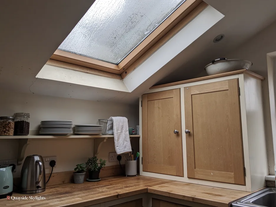 Pine roof window with misted glass above a kitchen dresser, kettle and plates