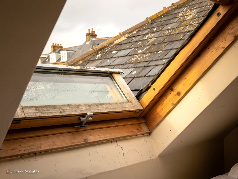 Tired pine roof window with a worn frame, open to a slate roof and sky