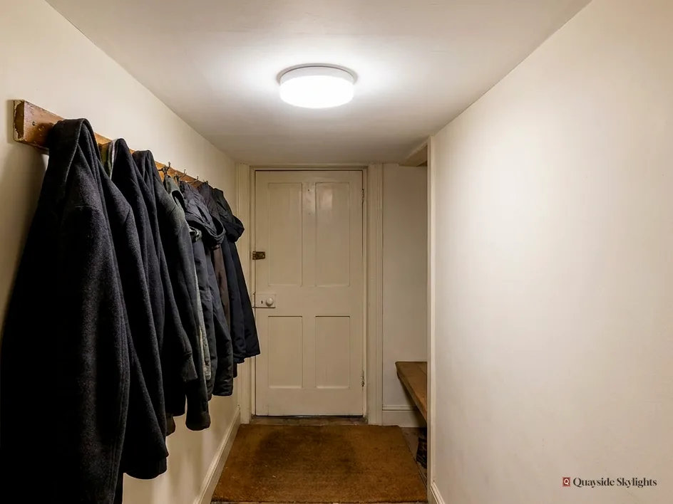 Entrance hallway with a round ceiling diffuser, coats on hooks and a panelled front door