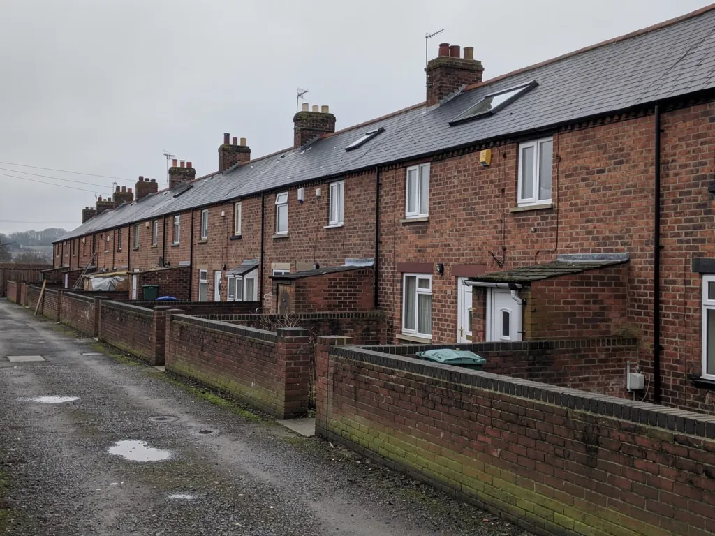 Back lane between rows of red brick terraced houses with walled yards