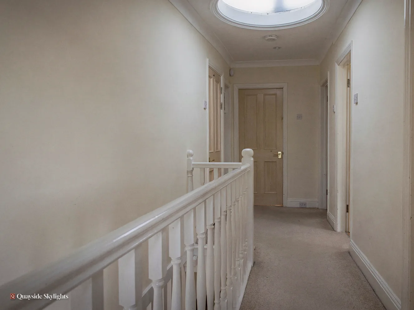 Upstairs landing with a sun tunnel diffuser, white balustrade and grey carpet