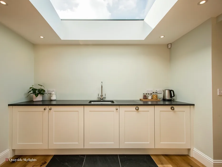 Cream kitchen units with a dark worktop beneath a frameless flat rooflight