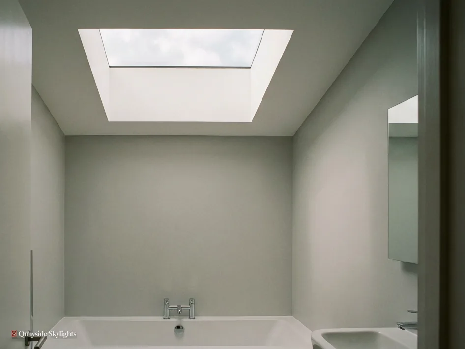 Pale green bathroom with a bath and basin beneath a flat rooflight