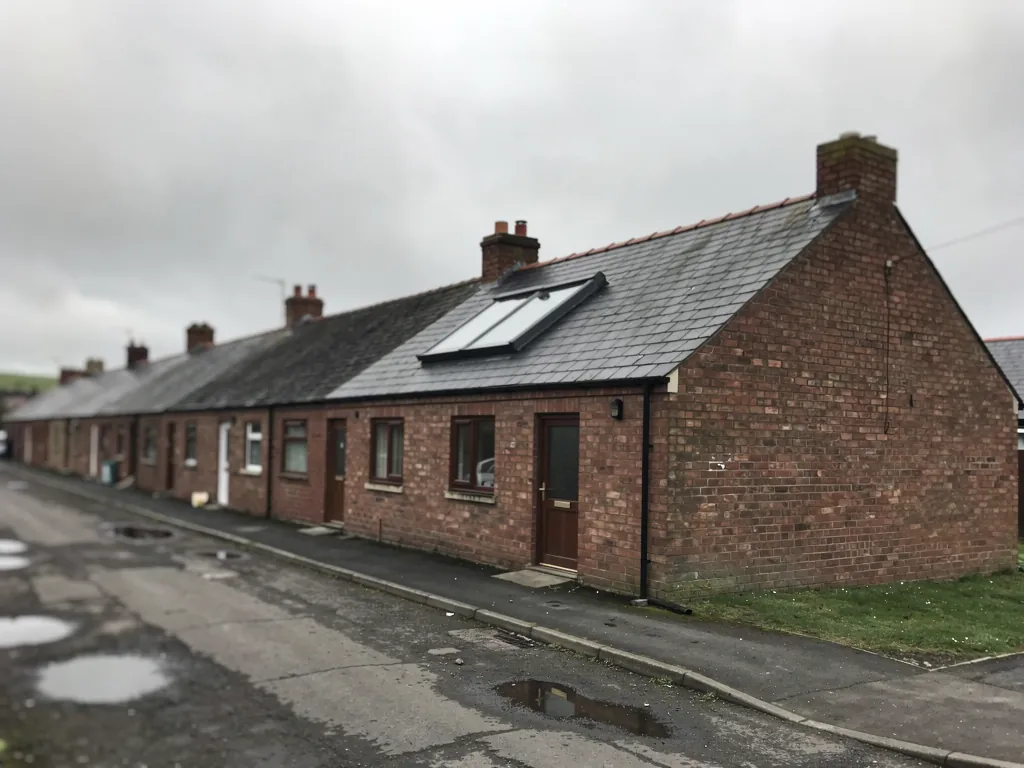 Row of single-storey brick terraced cottages with a roof window beside a lane
