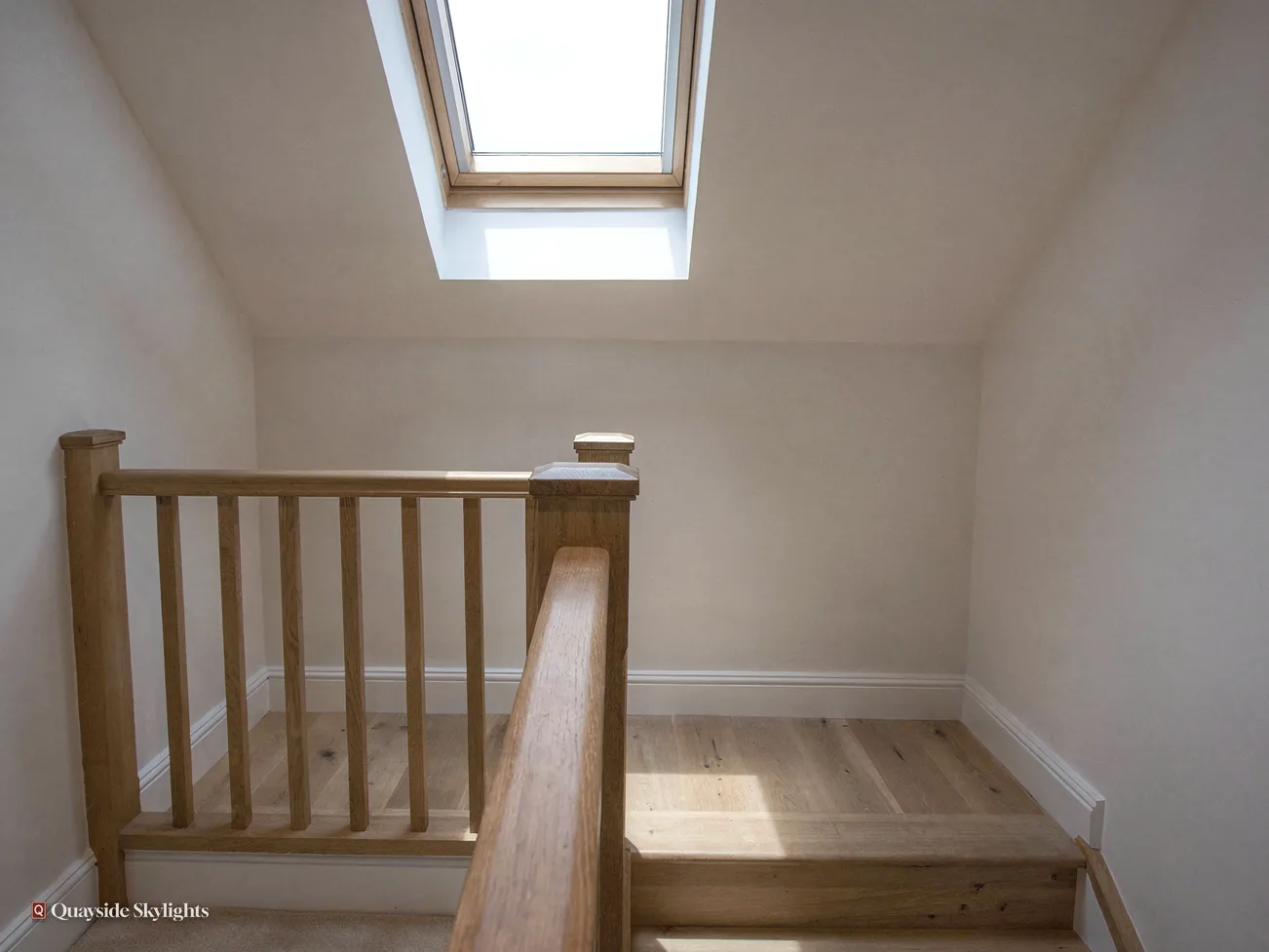 Bare landing under a small roof window with a timber balustrade and pine floor