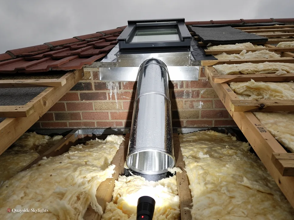 Sun tunnel tube passing through loft insulation between rafters under a tiled roof