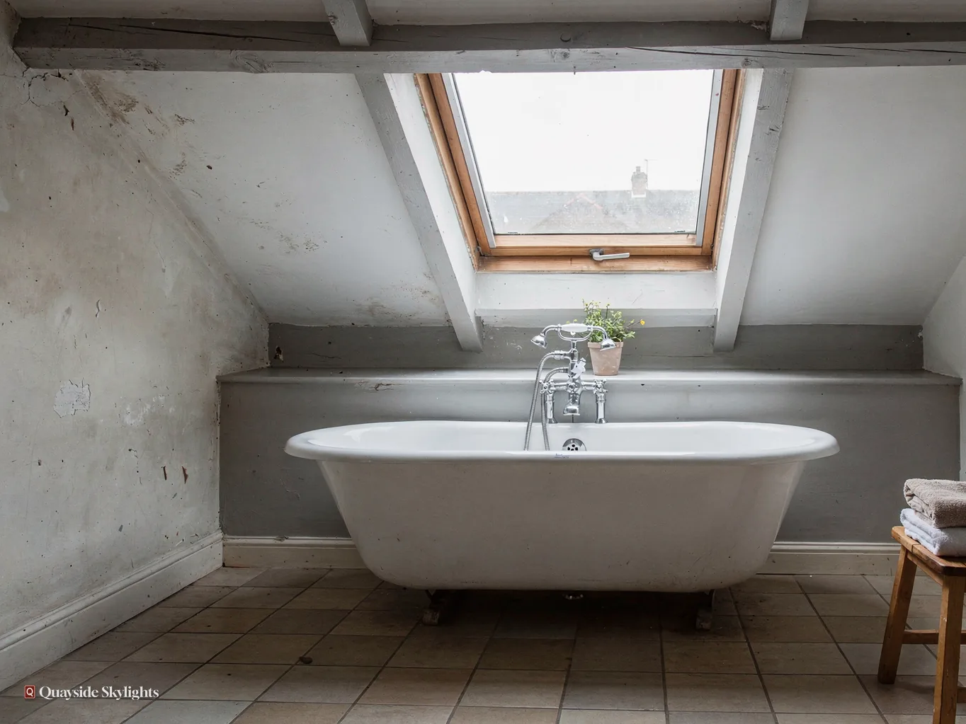 Roll-top bath under a pine roof window in a pale tiled bathroom