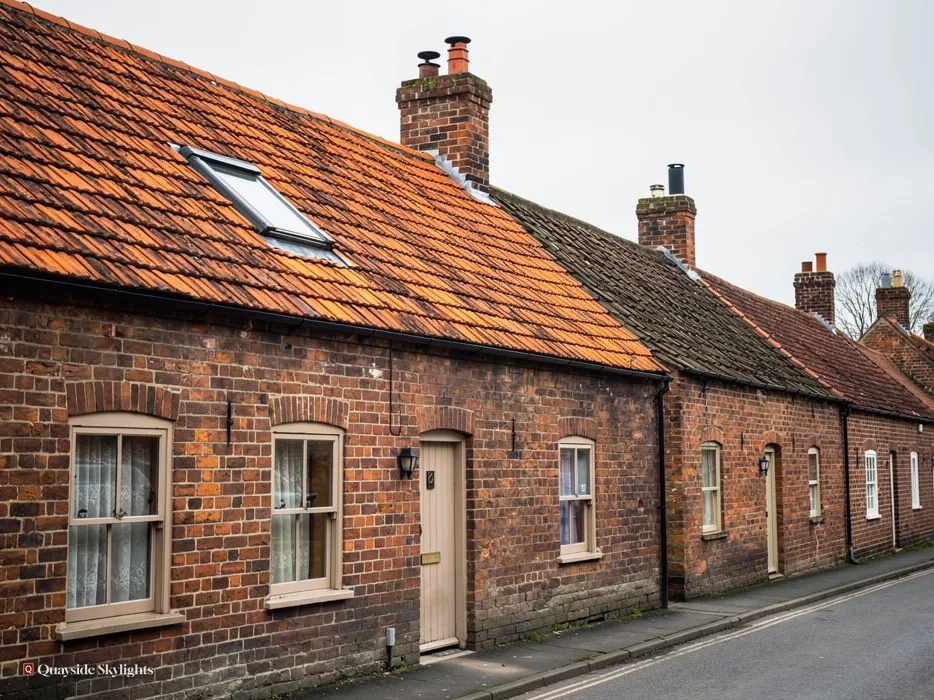 Brick cottages with orange pantile roofs, chimneys and a roof window