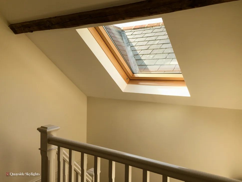 Stair landing with a pine roof window beneath a dark ceiling beam