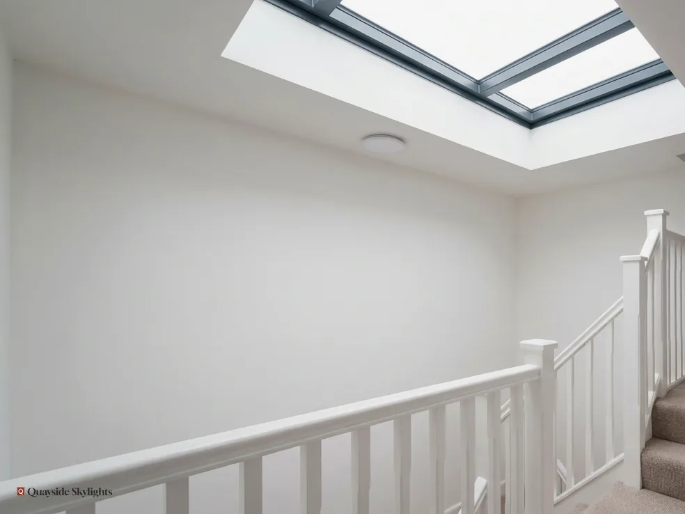 White landing with a painted balustrade beneath a frameless flat rooflight