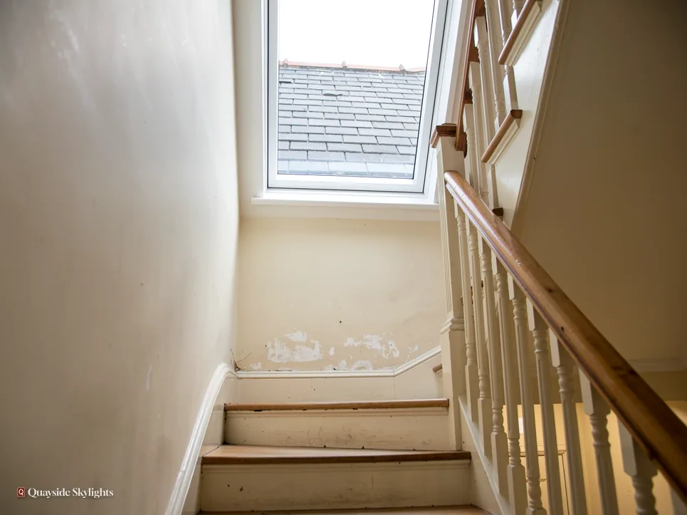 Stairwell with stained walls rising to a small roof window