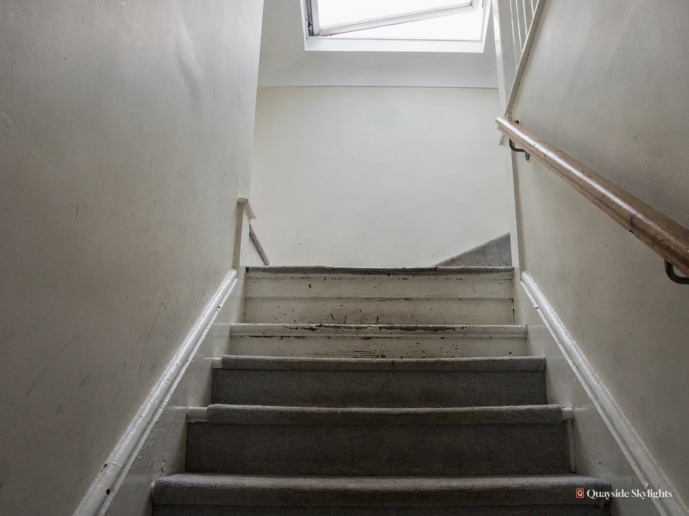 Narrow stairs with worn carpet climbing towards a rooflight