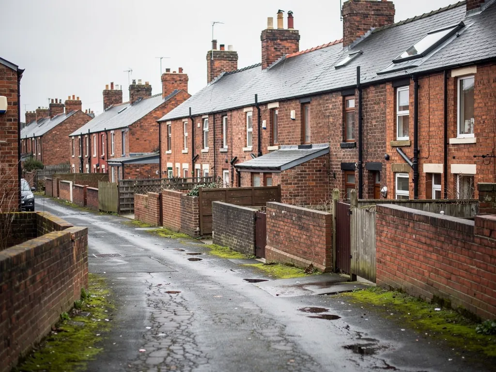 Wet back lane between brick terraced houses and yard walls