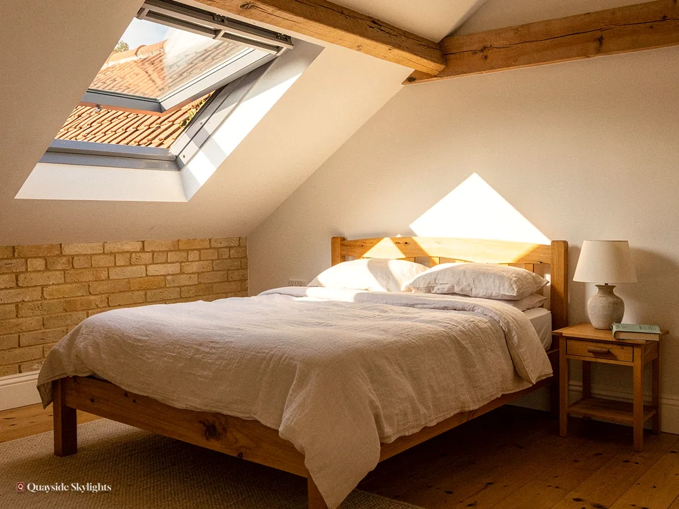 Loft bedroom with sunlight through an open roof window onto a stone wall