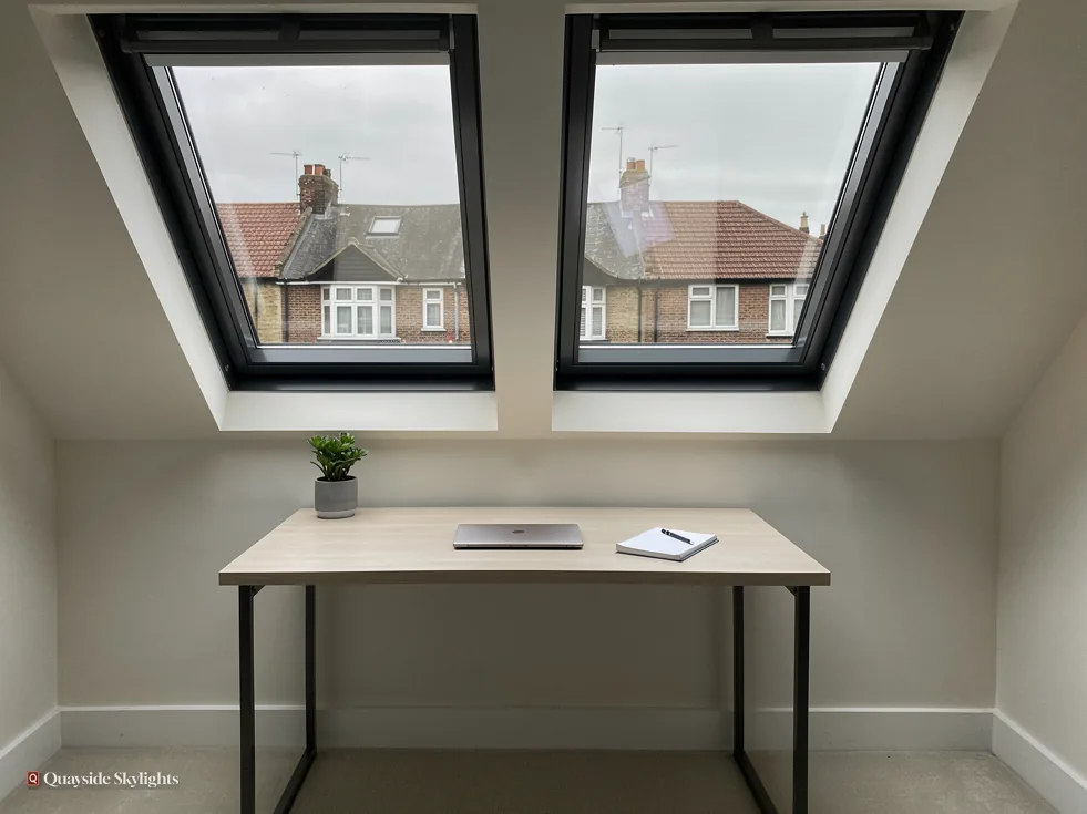 Desk beneath two black-framed roof windows overlooking neighbouring houses