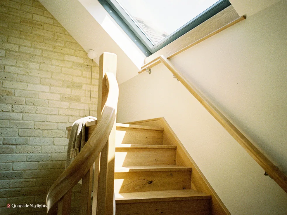 Timber staircase lit by a rooflight beside a painted brick wall