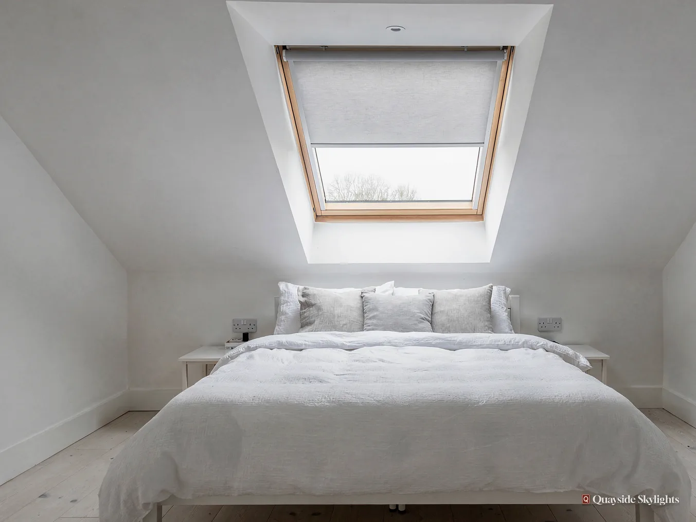 Bedroom with a grey blind half down on a roof window above the bed