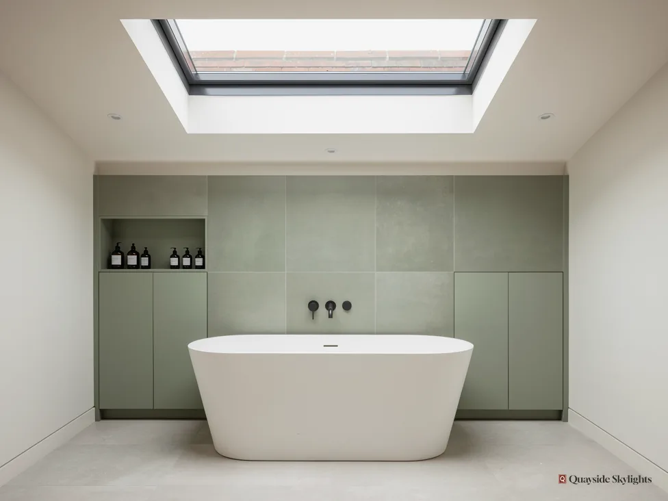 Freestanding bath against sage green cabinetry under a flat rooflight