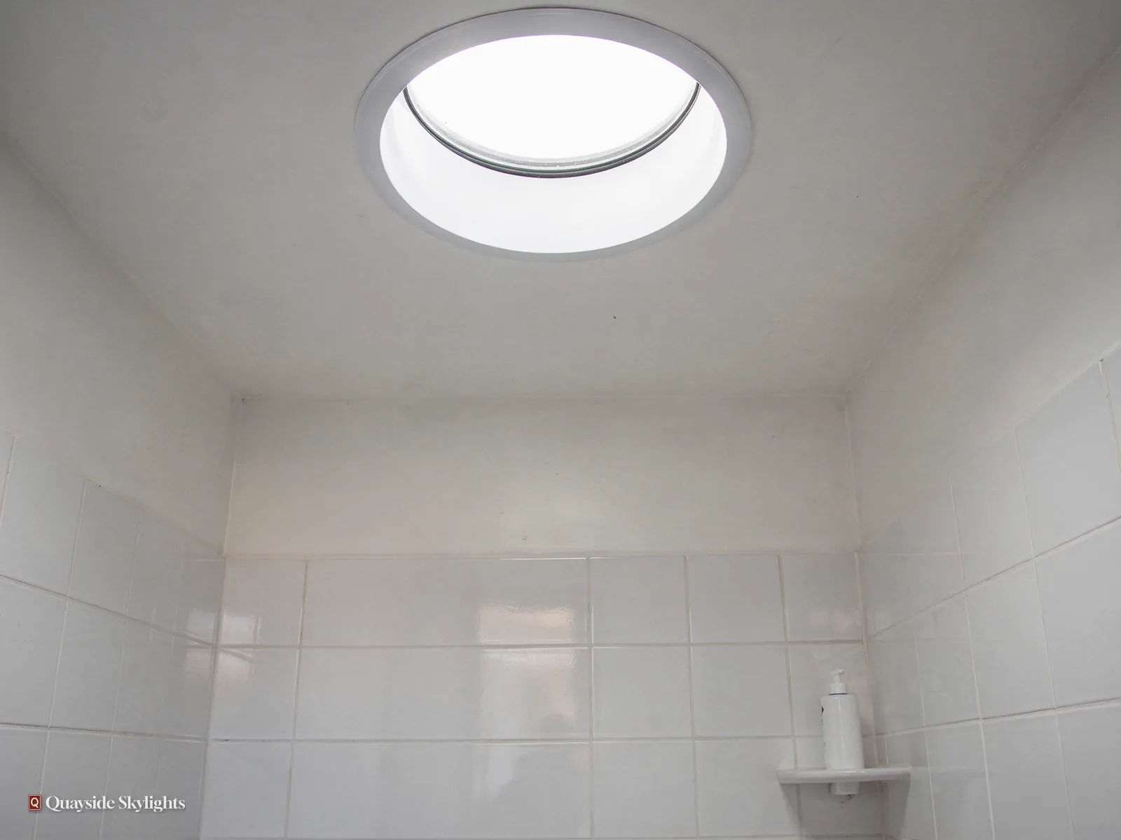 White tiled room with a round sun tunnel diffuser in the ceiling