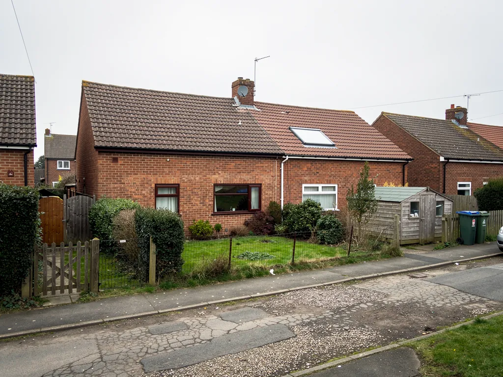 Brick bungalow with a roof window, front garden and cracked road