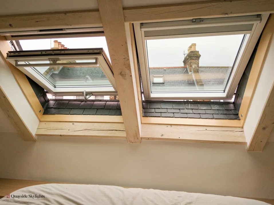 Two pine roof windows open towards a chimney above the foot of a bed