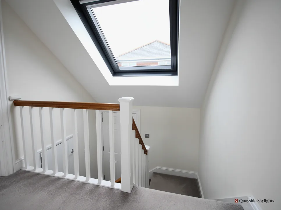 White painted staircase and landing lit from above by a dark-framed roof window