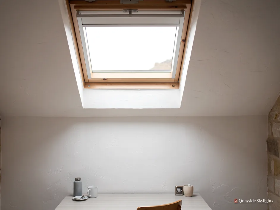 Room with a roof window and blind above a table with cups