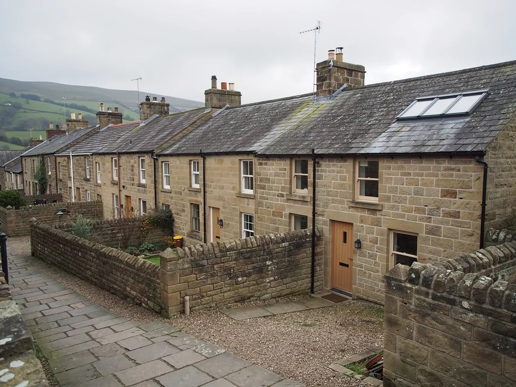 Stone terraced houses with roof windows and walled yards, hills beyond
