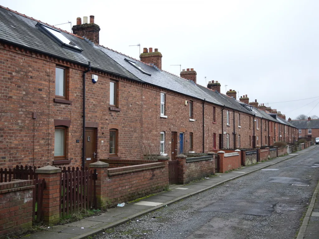 Long row of brick terraced houses with railings along a lane