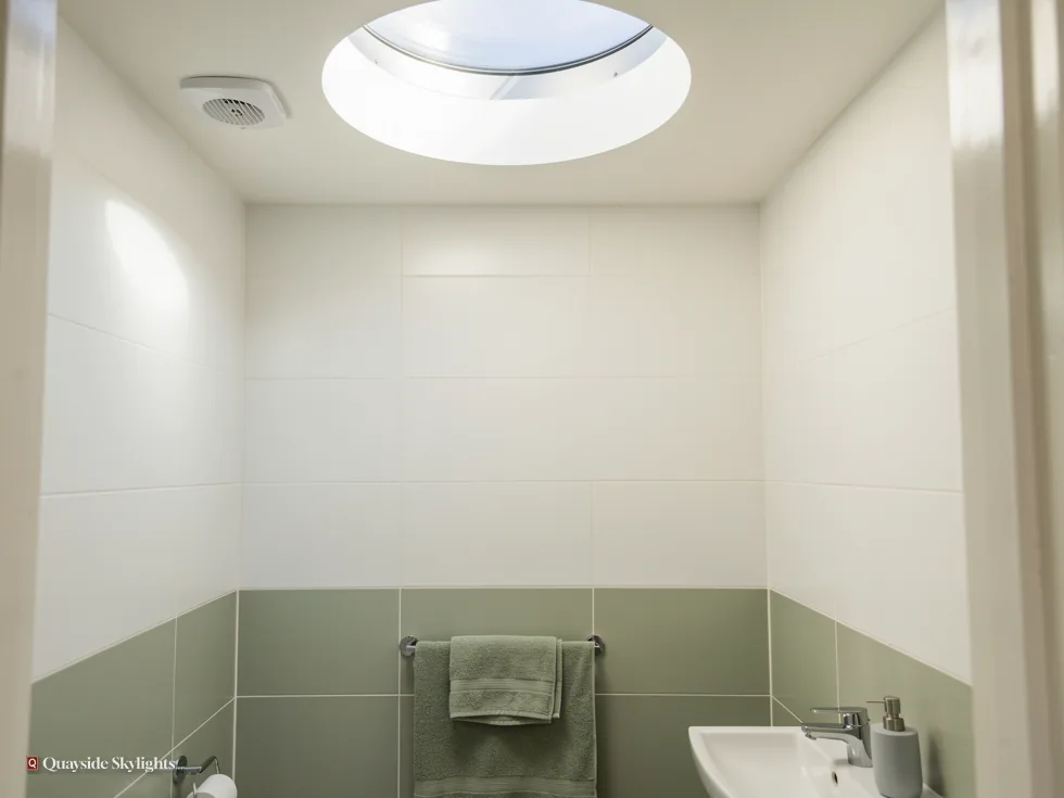 White bathroom with sage tiles and a basin under a round sun tunnel