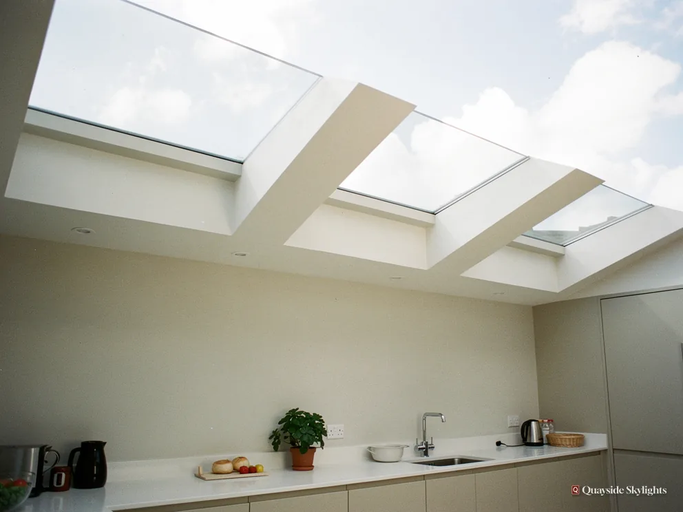 Kitchen worktop with a sink and plant under three flat rooflights