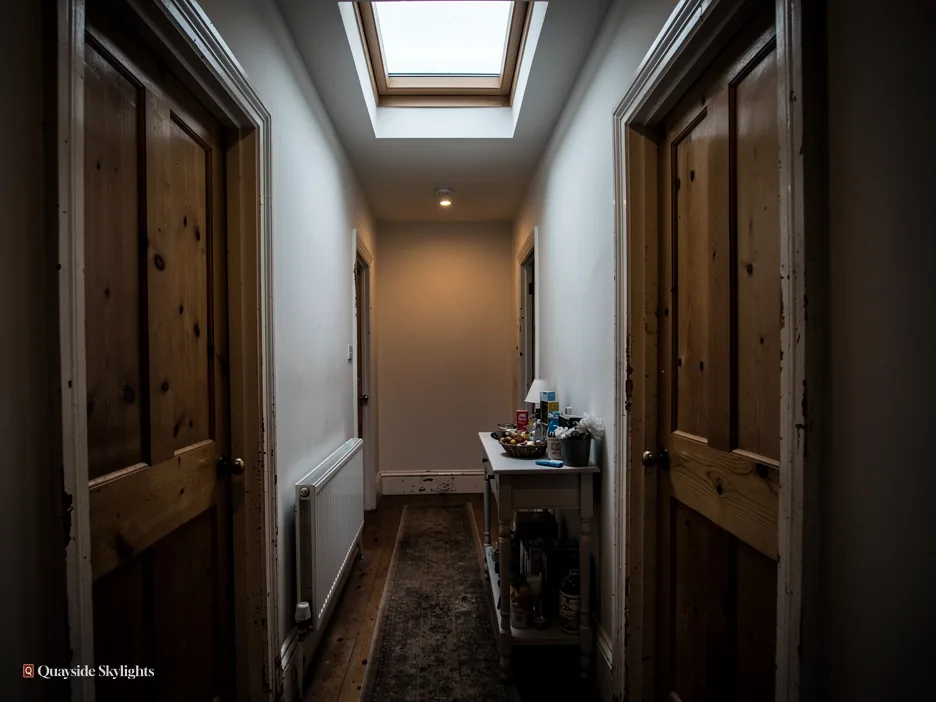 Dark corridor between timber doors with a rooflight at the far end