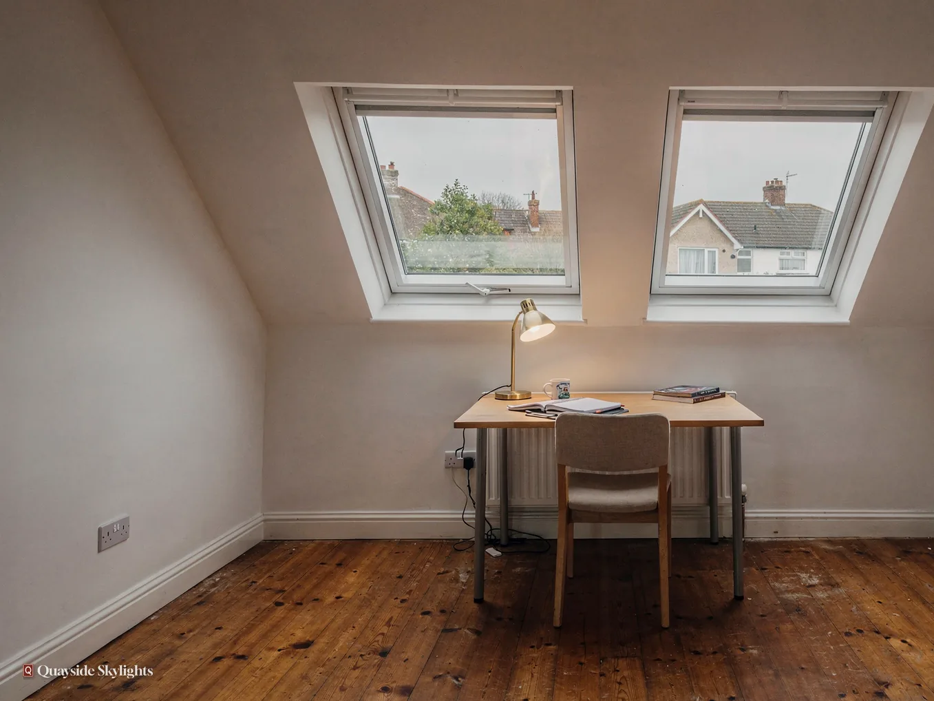 Desk and chair beneath two roof windows on a timber floor