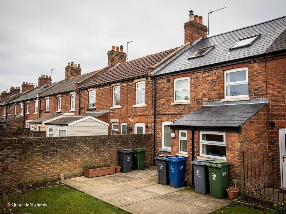 Rear of brick terraced houses with wheelie bins in a paved yard