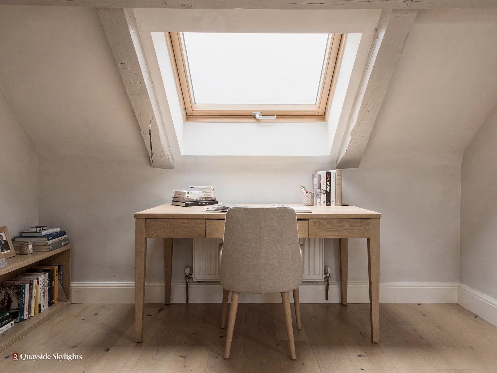Writing desk and upholstered chair under a roof window in a white loft room