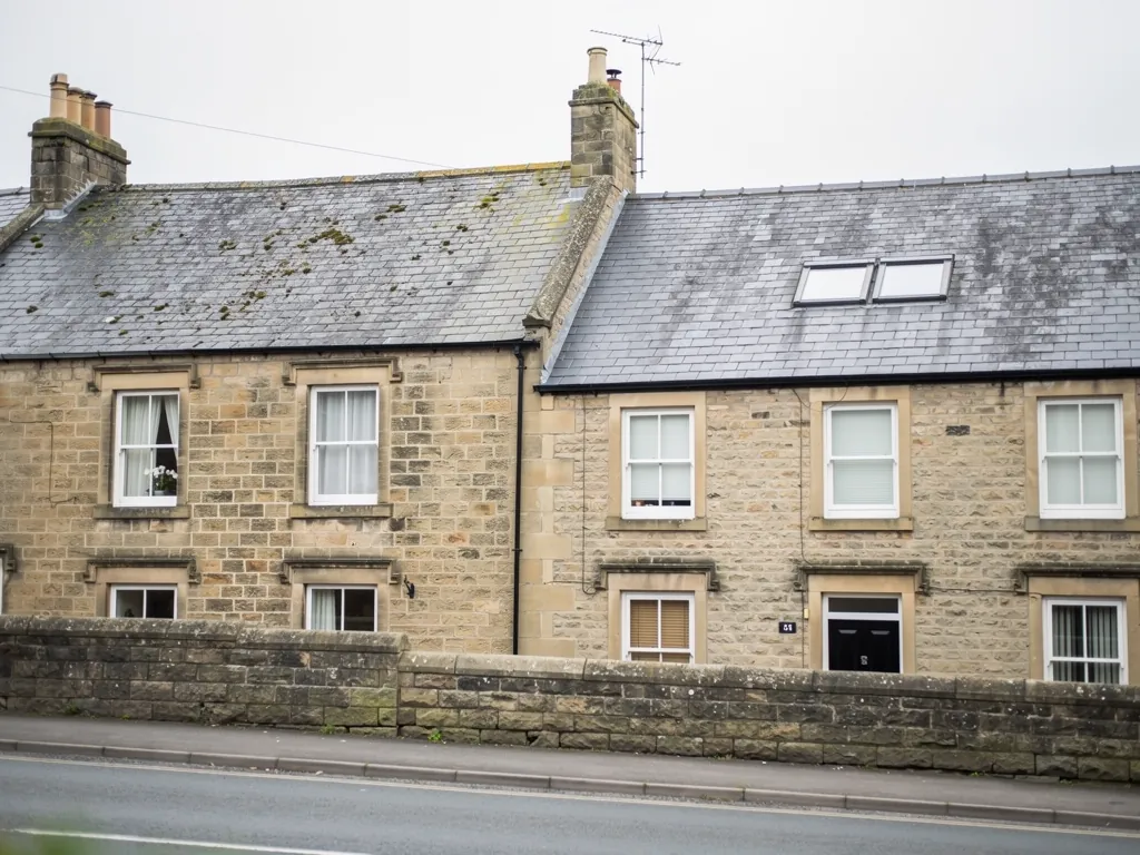 Sandstone terraced houses with roof windows behind a low stone wall