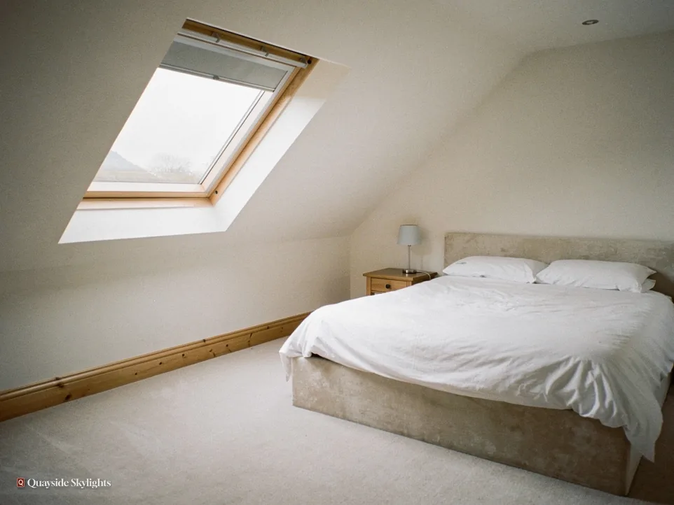 Bedroom with a roof window and blind above a made double bed