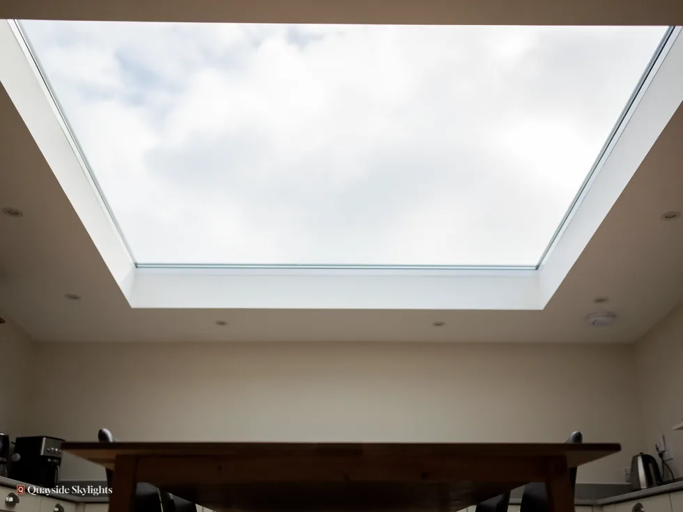 Frameless glass rooflight seen from below with cloudy sky above